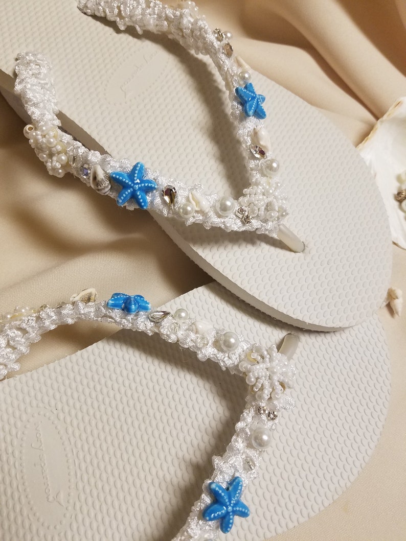 May include: White flip flops with a white crocheted strap decorated with blue starfish, white pearls, and silver beads.