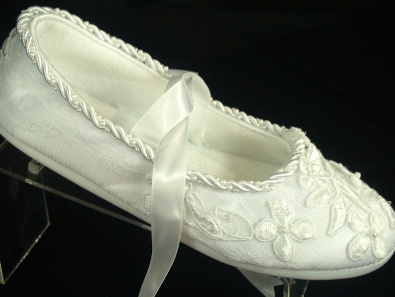 May include: White satin slipper with a white satin ribbon and pearl trim. The slipper is decorated with white embroidered flowers.