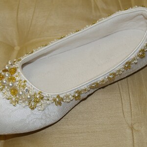 May include: White satin bridal slipper with gold and pearl embellishments.