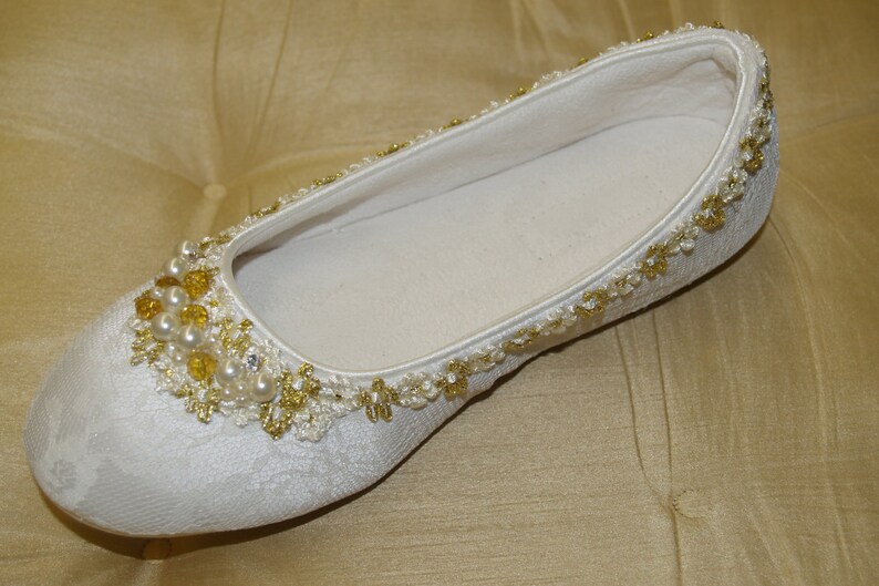 May include: White satin bridal slipper with gold and pearl embellishments.