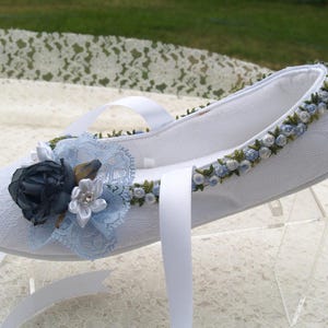 May include: White satin slipper with blue and green floral embroidery. The slipper has a white satin ribbon and a blue and white floral embellishment.