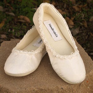 May include: A pair of white satin bridal slippers with a beaded trim and a label that reads "NewBrideCo."
