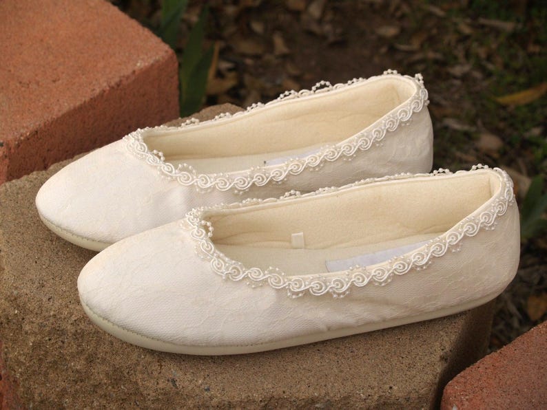 May include: A pair of white satin slippers with a delicate beaded trim. The slippers have a rounded toe and a low heel.
