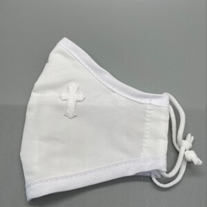 May include: White face mask with a white embroidered cross on the front. The mask has white trim and adjustable white cords. The mask is made of a soft, breathable fabric.