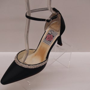 May include: Black satin heeled shoe with a rhinestone trim around the toe and an ankle strap. The shoe has a label that reads "Special Occasions" with a pink rose.