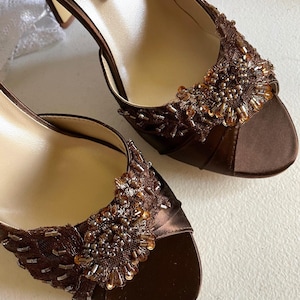 May include: A pair of brown satin heeled shoes with beaded embellishments. The shoes have a peep toe and a delicate lace design.
