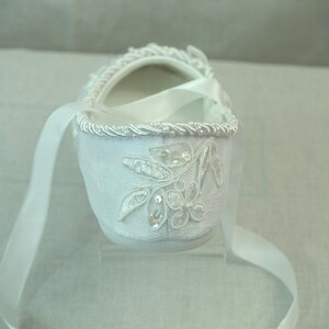 May include: White satin baby shoe with a white ribbon and a floral design with rhinestones.