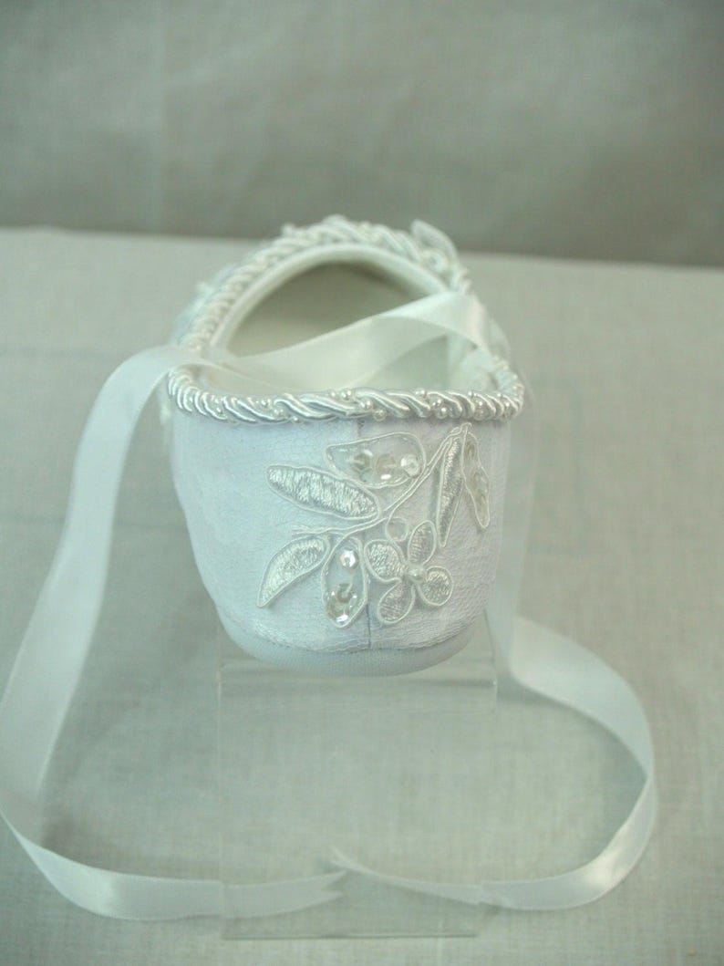 May include: White satin baby shoe with a white ribbon and a floral design with rhinestones.