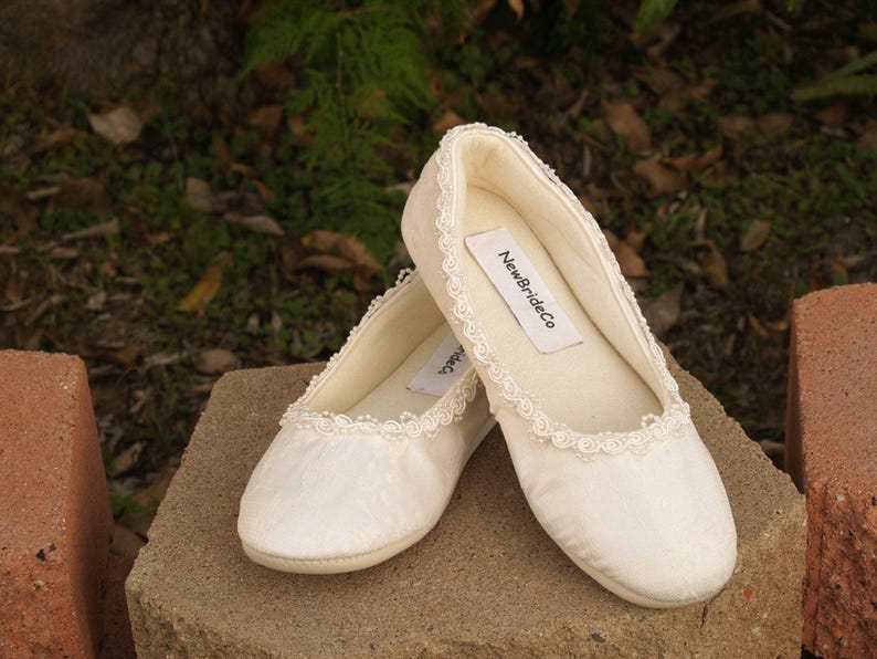 May include: Two pairs of white satin ballet flats with lace trim. The flats have a label that reads "NewBrideCo."