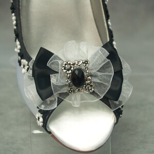 May include: White satin bridal shoes with a black satin bow and a silver and black jeweled embellishment.