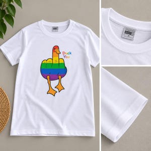 May include: A white short-sleeve t-shirt featuring a graphic of a duck with rainbow-colored feathers making a hand gesture. The text "Duck You" is printed in small colorful letters next to the duck. The inner neck label reads "TALENTO BASICO M".