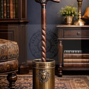 Può includere: Un bastone da passeggio con un fusto in legno marrone scuro dal design intrecciato e un'impugnatura in metallo a forma di testa di coniglio. Il bastone poggia su un supporto cilindrico in ottone con un emblema a testa di leone.
