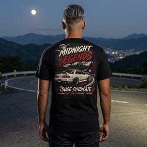 May include: Black t-shirt featuring a car graphic with the text "Midnight Legends" and "Touge Syndicate." The design includes a white car on a winding road, set against a mountain backdrop. The shirt also has Japanese text.