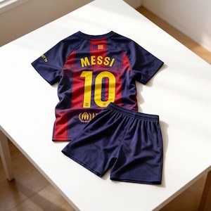 May include: A navy blue and red soccer jersey and shorts set. The jersey features the name "MESSI" and the number "10" in yellow. The shorts are navy blue. The set is displayed on a white surface.