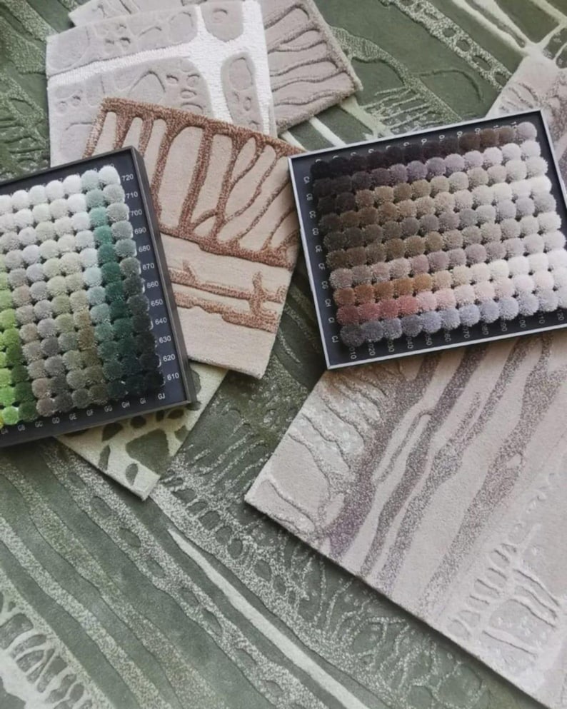 Pu&ograve; includere: Due cartelle colori rettangolari con una griglia di piccoli campioni di tessuto trapuntato circolare in varie tonalit&agrave; di verde e marrone, disposte sopra diversi campioni di tessuto testurizzato con motivi astratti in beige, grigio e verde.