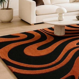 Pu&ograve; includere: Un tappeto rettangolare caratterizzato da una texture a pelo alto e basso con un audace motivo ondulato in tonalit&agrave; alternate di arancione bruciato e nero profondo. Il design &egrave; composto da linee fluide e organiche che creano movimento.