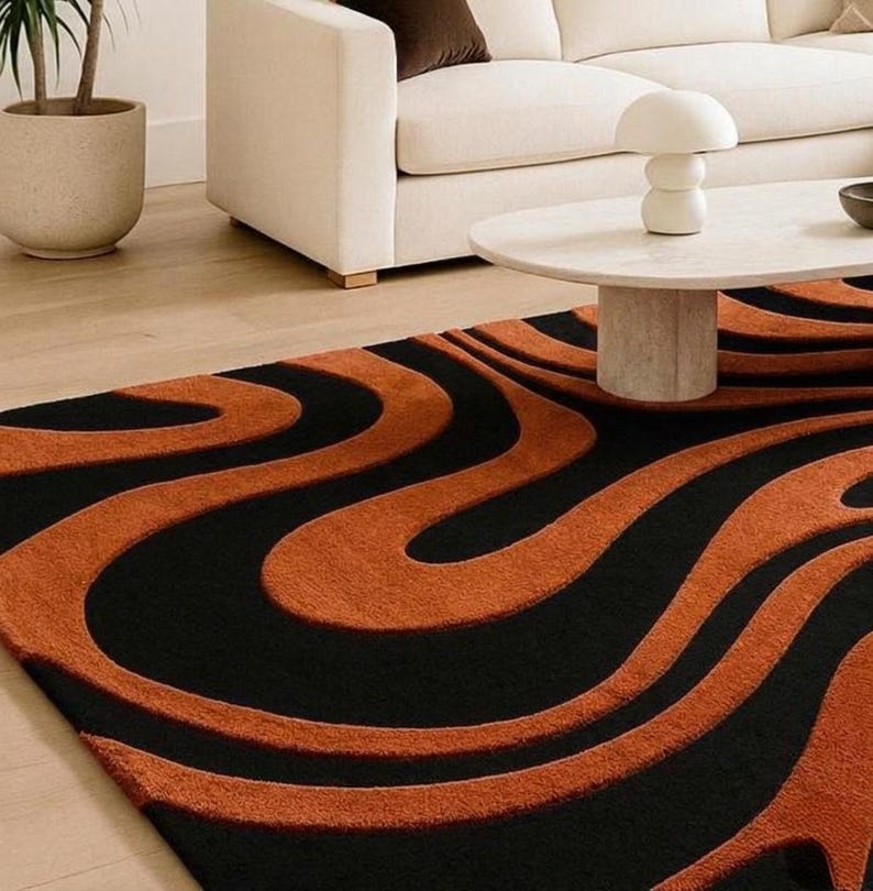 Pu&ograve; includere: Un tappeto rettangolare caratterizzato da una texture a pelo alto e basso con un audace motivo ondulato in tonalit&agrave; alternate di arancione bruciato e nero profondo. Il design &egrave; composto da linee fluide e organiche che creano movimento.
