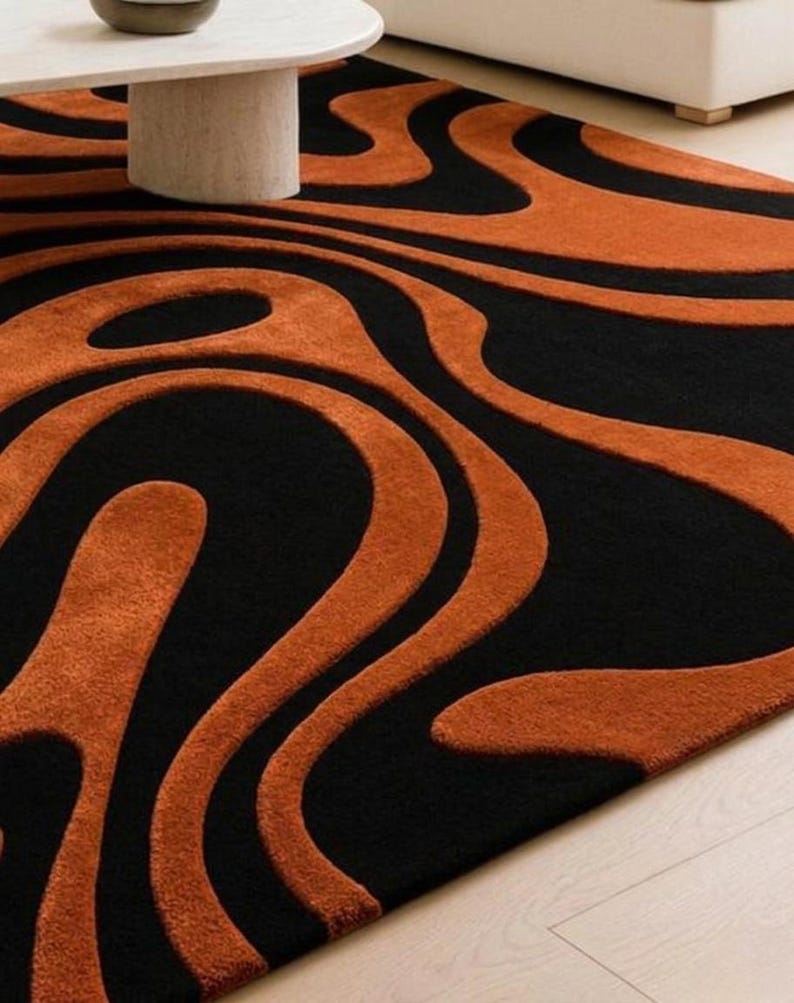 Pu&ograve; includere: Un tappeto rettangolare caratterizzato da un motivo astratto ad alto contrasto con forme organiche fluide in nero profondo e arancione bruciato. Il design &egrave; composto da spesse linee ondulate che creano un senso di movimento sulla superficie.