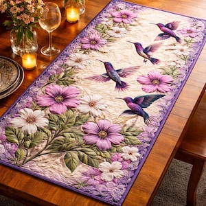 May include: A rectangular table runner featuring a floral and hummingbird design. The runner has a cream-colored background with embroidered purple and white flowers, green leaves, and several hummingbirds in flight. The border is a darker purple.