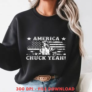 May include: Black sweatshirt featuring a graphic of the American flag with a portrait and the text "AMERICA CHUCK YEAH!". The design is in white, with stars and stripes, and the image of a person holding two guns.