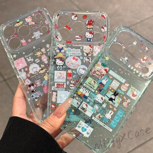 Puede incluir: Fundas transparentes para tel&eacute;fono con dise&ntilde;os coloridos de Hello Kitty y otros personajes de dibujos animados. Las fundas presentan varias im&aacute;genes de Hello Kitty, conejitos y otros personajes lindos. Las fundas est&aacute;n en la mano de una persona.