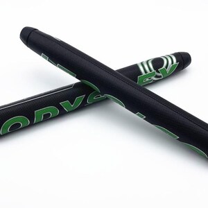 May include: Two black golf putter grips with green lettering and accents are displayed against a white background. The grips are cylindrical and textured, with the word "ODYSSEY" visible. One grip is positioned over the other.