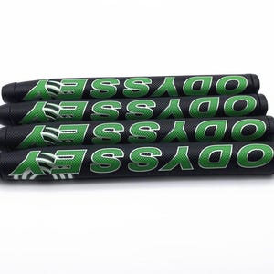May include: Four black golf putter grips with the word "ODYSSEY" in green block letters. The grips have a textured surface and a green and white logo. The grips are stacked on top of each other.