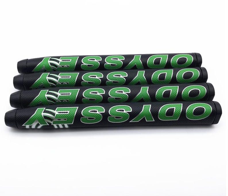 May include: Four black golf putter grips with the word "ODYSSEY" in green block letters. The grips have a textured surface and a green and white logo. The grips are stacked on top of each other.
