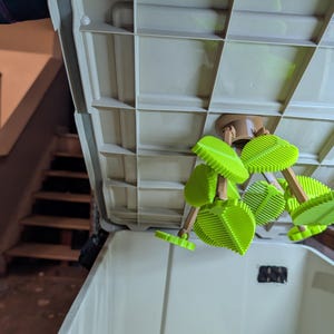 May include: A light beige storage container with a grid-like lid. Attached to the lid are several green leaf-shaped cleaning tools with wooden handles. The container is open, revealing the interior.