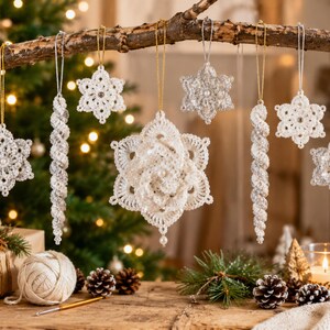 May include: A collection of white crocheted snowflake and icicle ornaments hanging from a wooden branch. The ornaments feature intricate lace patterns, small white beads, and metallic gold or silver hanging strings, creating a festive display.