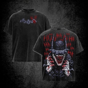 May include: Black t-shirt featuring a graphic of a character with a menacing grin and the word "HA" repeated. The front of the shirt has a pixelated design with the word "MAN" in red. The shirt has a vintage, distressed look.