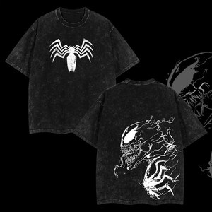 May include: Black acid wash t-shirt featuring a white Venom spider logo on the front and a Venom graphic on the back. The t-shirt has a crew neck and short sleeves. The design is a graphic print.