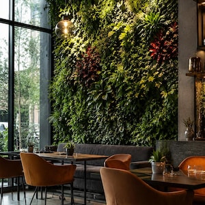 Könnte beinhalten: Innenaufnahme eines Restaurants mit einer lebenden Wand. Der Raum verfügt über braune Samtstühle, dunkle Tische und eine lange, dunkelgraue Bank. Große Fenster bieten einen Blick auf Bäume. Kugelförmige Pendelleuchten beleuchten den Essbereich.