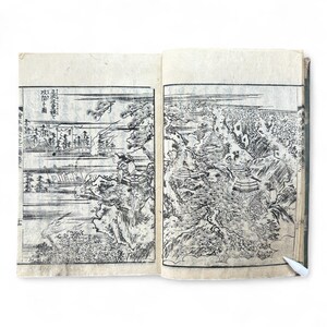 Puede incluir: Libro abierto con dos ilustraciones en blanco y negro. La página izquierda representa un paisaje con árboles y figuras. La página derecha muestra una detallada escena de montaña con edificios y árboles. El libro tiene páginas envejecidas y texturizadas.