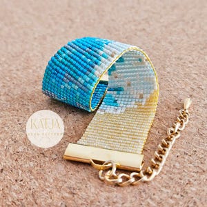 May include: A beaded bracelet with a blue and white pattern, transitioning to gold beads. The bracelet has a gold clasp and chain. The text "KATJA" and "BEAD PATTERNS" is visible on the image.