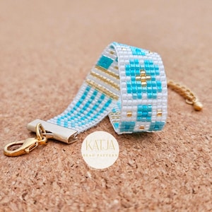 May include: A beaded bracelet with a white base, featuring a geometric pattern in turquoise and gold. The bracelet has a gold clasp and a matching gold chain. The brand name "KATJA BEAD PATTERN" is visible on a white circle.