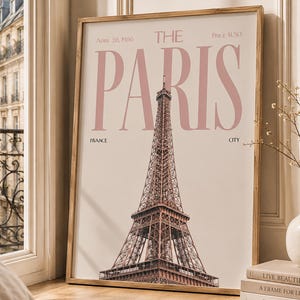 Op de afbeelding: Een ingelijste verticale wandkunstprint met de Eiffeltoren in het midden en de grote roze tekst THE PARIS erboven. De print bevat de tekst April 28, 1986, Price $1.50, France en City op een lichtbeige achtergrondkleur.
