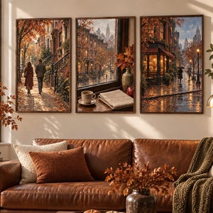 May include: A triptych of framed wall art prints depicting autumn city scenes, featuring a couple walking on a pavement, a window view with a coffee cup and book, and a rainy street with glowing lights, displayed above a brown leather sofa.