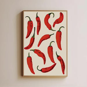 Puede incluir: Una impresión artística enmarcada que presenta una colección de pimientos rojos vibrantes sobre un fondo crema. Los pimientos tienen tallos verdes y están dispuestos en un patrón repetitivo. El marco es de color marrón cálido.