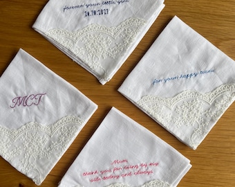May include: Four white square handkerchiefs with lace trim. One features blue embroidery reading Dad forever your little girl 24.10.2027, one has purple MCT initials, one says for your happy tears in blue, and one has pink text Mum thank you for being by my side today and always.