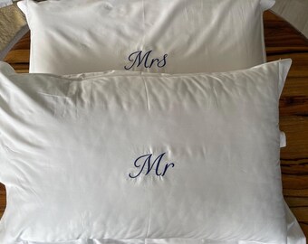 May include: Two white rectangular pillowcases featuring centered embroidery in dark blue script. The top pillowcase displays the text "Mrs" and the bottom pillowcase displays the text "Mr" in a matching elegant font style.