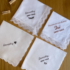 May include: Four white fabric handkerchiefs with embroidered text and lace or scalloped edges. Three feature the name Dorothy with dates 1940-2026 and symbols, while one features the text Forever in our hearts Dad 1945-2025.