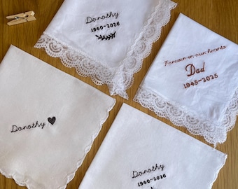 May include: Four white fabric handkerchiefs with embroidered text and lace or scalloped edges. Three feature the name Dorothy with dates 1940-2026 and symbols, while one features the text Forever in our hearts Dad 1945-2025.