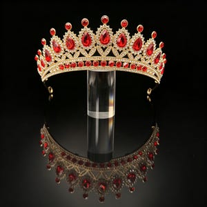 Könnte beinhalten: Ein goldfarbenes Metall-Diadem mit einer Reihe von tropfenförmigen roten Kristallen und kleineren runden roten Steinen. Die Krone ist mit zahlreichen klaren weißen Strasssteinen verziert, die entlang des Bandes und um jedes Element angebracht sind.