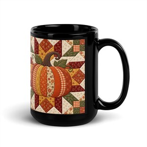 May include: A black ceramic mug featuring a printed graphic of a pumpkin composed of various fabric-like patterns in shades of orange, yellow, and red, set against a background of geometric quilt-style blocks in autumn colours with green leaves.