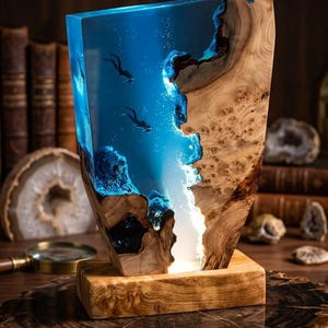 May include: A decorative lamp with a blue resin design depicting divers and bubbles, set within a wooden frame. The lamp, with its natural wood tones, is illuminated from within, creating an underwater effect. The lamp sits on a wooden base, adding to its aesthetic appeal.