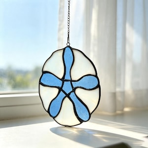 Peut inclure: Un attrape-soleil en vitrail en forme de dollar des sables, composé de cinq segments en verre bleu translucide disposés en étoile sur des panneaux en verre blanc opaque, le tout assemblé par des lignes de soudure noires et une chaînette.