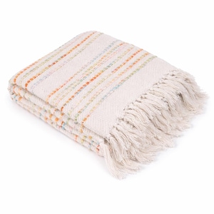May include: A folded woven throw blanket in an off-white cream color featuring thin, vertical stripes in muted orange, yellow, and light blue. The blanket has a textured, nubby weave and is finished with long, matching cream-colored fringe.