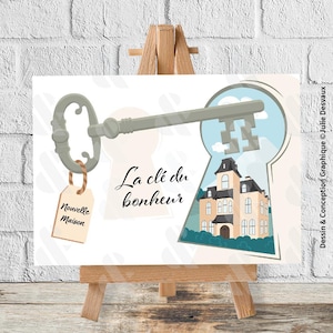 May include: A decorative print on an easel features a key design with a keyhole revealing a house. The key has a tag that says "New Home". The text "La clé du bonheur" is also on the print.