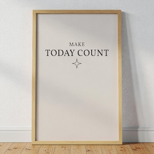 Puede incluir: Un cartel enmarcado con las palabras "MAKE TODAY COUNT" en texto negro, con un símbolo de estrella debajo. El marco es de color marrón claro y el fondo es de color beige claro. El cartel está apoyado contra una pared blanca sobre un suelo de madera.